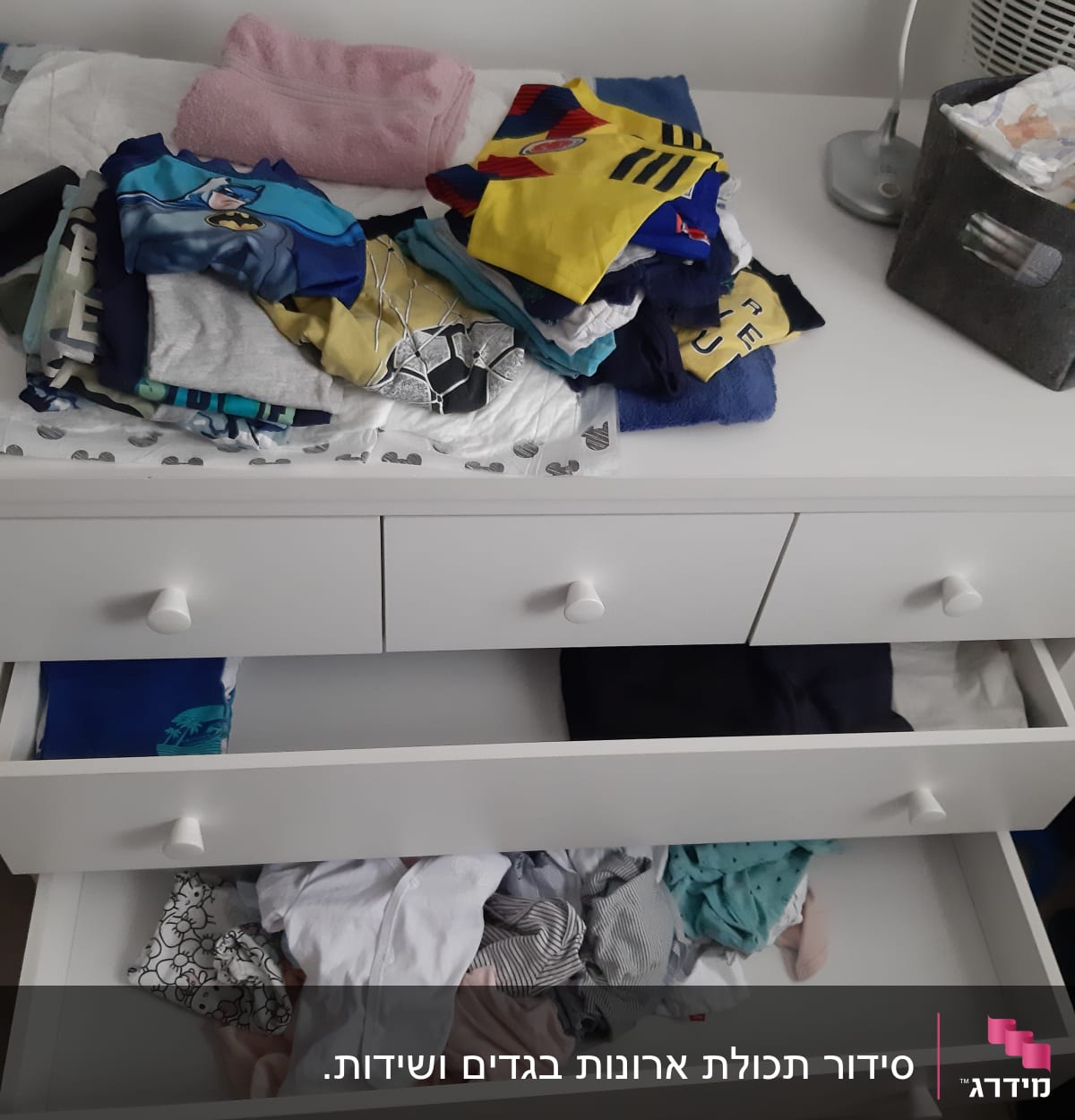מגירות עם בגדים מקופלים ומפוזרים על שידה לבנה